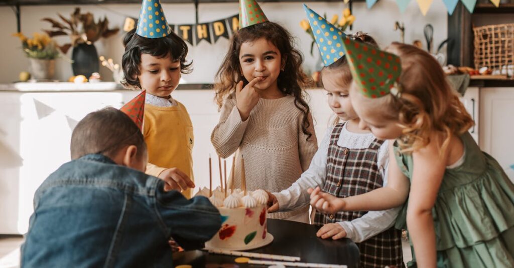 A group of children celebrating a birthday with cake and party hats indoors.